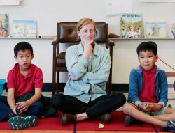 A teacher scholar sits with her students on the rug
